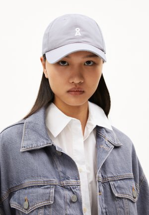 Gray baseball cap with a white embroidered logo. The model wears a denim jacket over a white shirt, emphasizing the cap's color and design.
