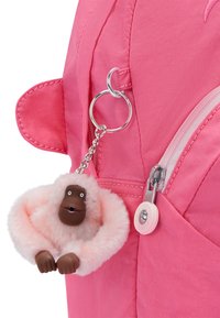 Den lyserøde rygsæk har en pelsagtig abe-nøglering med en fluffy, lyserød krop og et brunt ansigt. Sølvhardware er fastgjort til lynlåsen.