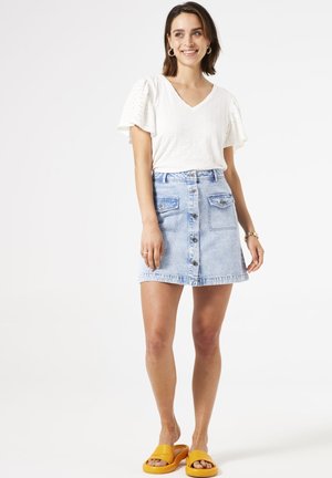 Witte textuur V-hals top met pofmouwen, gecombineerd met een lichtblauwe denimrok met een voorpaneelknopen en twee voorzakken. Gele slippers.