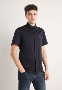 Camicetta blu scuro a maniche corte con colletto e un piccolo logo bianco "BOSS" sul lato sinistro del petto, realizzata in tessuto morbido.