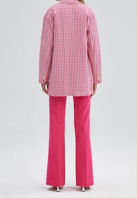 Roze-wit geruit oversized blazer met lange mouwen en knoopdetails, gecombineerd met roze high-waisted wijde broekspijpen.