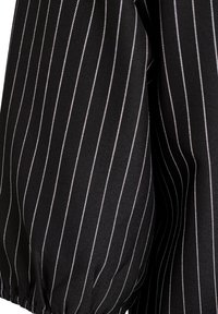 Musta kangas, jossa on pystysuorat valkoiset raidoitukset ja kootut joustavat yksityiskohdat hemillä, näyttäen tekstuuria ja vaatekappaleen yksityiskohtia.