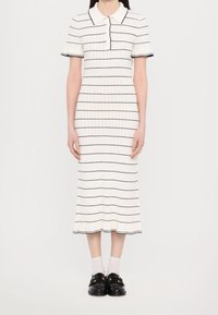 Robe polo rayée en blanc avec des lignes horizontales navy, à manches courtes et avec un ourlet légèrement évasé. Portée avec des chaussettes blanches et des mocassins noirs.