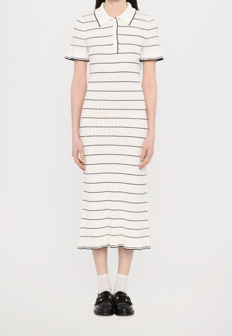 Robe polo rayée en blanc avec des lignes horizontales navy, à manches courtes et avec un ourlet légèrement évasé. Portée avec des chaussettes blanches et des mocassins noirs.