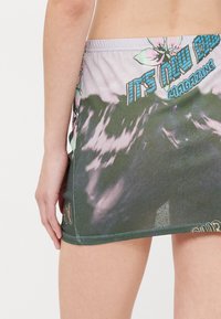 Falda con estampado floral que presenta una cintura elástica, predominantemente gris con acentos en verde y rosa, y texto decorativo en el dobladillo.