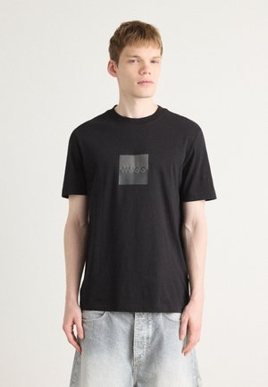 T-shirt nera in cotone con logo quadrato nero opaco al centro, con la scritta "HUGO". Maniche corte e scollo rotondo.