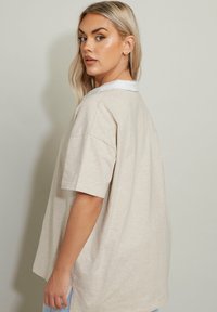 Beige oversize t-shirt med korta ärmar och vit krage, med en mjuk textur och avslappnad passform, sedd bakifrån.