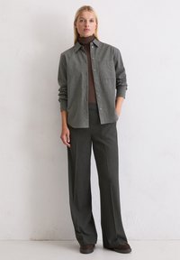 Γκρι πουκάμισο με κουμπιά σε μαλακό ύφασμα με τσέπη στο στήθος, συνδυασμένο με καφέ ζιβάγκο και σκούρες παντελόνες με ρίγες. Καφέ παπούτσια προσθέτουν αντίθεση.