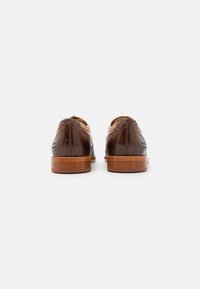 Scarpe in pelle marrone con perforazioni decorative e dettagli in tonalità nocciola. Forma arrotondata con tacco in legno, viste da dietro.