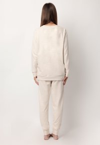 Conjunto de loungewear de algodón beige, que incluye una camiseta de manga larga con cuello redondo y pantalones de chándal a juego con puños en los tobillos.