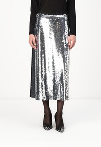Zilveren pailletjes midi-rok met een rechte snit en een zwarte stof tailleband, gecombineerd met zwarte hakken en doorzichtige panty's.