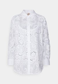 Blouse blanche à manches longues, ornée de broderies florales découpées et d'un col classique. Boutons à l'avant et ourlet droit.