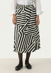 Jupe midi rayée noir et blanc avec taille élastique, présentant des motifs géométriques et un tissu texturé. Chaussures noires plates portées.