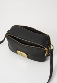 Borsa a tracolla nera in pelle con cerniere dorate e una placca con logo metallico. Presenta due scomparti e una tracolla rimovibile. Texture liscia.