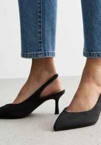 Czarne szpilki typu slingback z ostro zakończonym noskiem. Wykonane z miękkiego materiału, z wąskim obcasem. Noszone z przyciętymi dżinsami.
