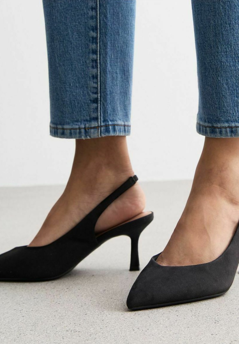 Czarne szpilki typu slingback z ostro zakończonym noskiem. Wykonane z miękkiego materiału, z wąskim obcasem. Noszone z przyciętymi dżinsami.