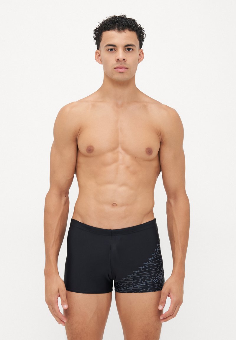 Schwarze Badeshorts aus glattem Material mit einem blauen Zickzackmuster an der Seite und einem elastischen Bund für hohen Tragekomfort.