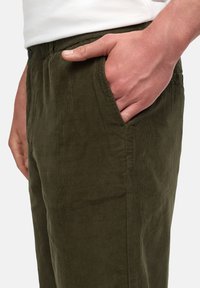 Pantalones de pana verde oliva con un corte holgado, que cuentan con bolsillos laterales y una textura visible gracias al tejido estriado.