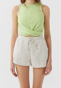 Haut sans manches vert clair avec un design à l'avant tordu, associé à un short léger en tissu gris clair avec un cordon de serrage et une coupe décontractée.