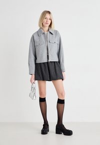 Grå vadderad ulljacka med två framfickor, ihop med svarta ränderade shorts, svarta knälånga strumpor och kraftiga svarta skor.