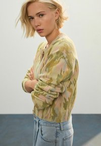 Cardigan tricotat ușor, cu un model de camuflaj în nuanțe de verde deschis, roz și bej. Include o gât rotund și tiv cu nervuri.