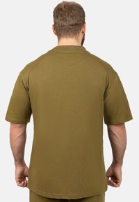 Chemise à manches courtes vert olive présentant une texture côtelée, un ourlet droit et des manches raglan, avec des coutures visibles aux épaules.