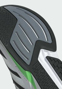 Čierna a šedá atletická podrážka so štruktúrovaným vzorom, hladkými šedými akcentmi, zelenými detailmi a hlbokými drážkami pre trakciu.