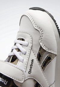 Baskets blanches Reebok avec dessus synthétique lisse, fermeture à lacets, accents texturés et semelle noire avec découpes latérales en motif.