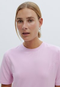 Helles rosa Baumwoll-T-Shirt mit kurzen Ärmeln und rundem Halsausschnitt. Verfügt über minimale Nahtdetails und eine glatte Textur. Keine Muster oder Akzente.