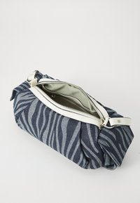 Jeansväska med zebra-mönster, vit läderrem och dragkedjestängning, med en mjuk grön innerfoder och rund form.
