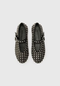 Chaussures Mary Jane en cuir noir avec des clous argentés, une sangle à boucle, un bout ovale et une tige texturée. Semelle plate avec un profil minimal.