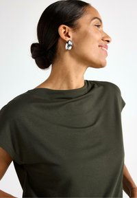 Olivenfarvet kortærmet top med draperet halsudskæring, parret med store sølvfarvede hoops øreringe. Glat stof med en afslappet pasform.