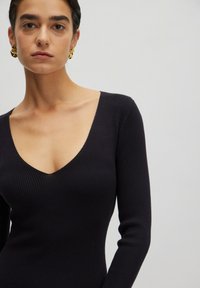 Zwart geribbelde longsleeve top met een diepe V-halsontwerp. Stevige textuur met een aansluitende pasvorm, die de halslijn en het bovenlichaam accentueert.