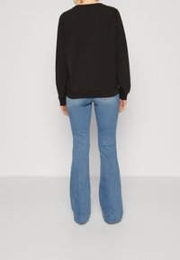Czarna bluza z długimi rękawami, zaokrąglonym dekoltem i luźnym krojem, zestawiona z jasnoniebieskimi rozkloszowanymi dżinsami o wyblakłym wykończeniu.