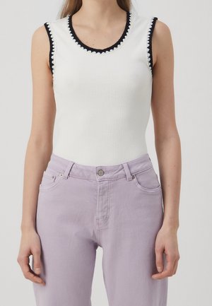 Biały prążkowany top na ramiączkach z granatową falbanką na dekolcie i rękawach, zestawiony z jasnofioletowymi dżinsami z klasycznymi okuciami.