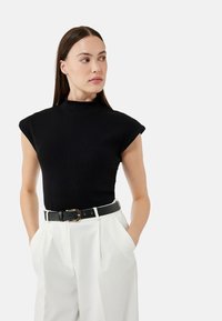 Svart ribbad ärmlös topp med hög halsringning. Matchad med högmidjade vita byxor och ett svart bälte med en guldbuckle.