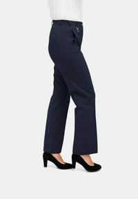 Navy kaki's met een lichte stretch, voorzien van een platte voorkant, zijzakken en een subtiel ruitpatroon. Hakken in het zwart passen mooi bij de outfit.