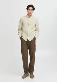 Lyse fargede stripete skjorte med knapper laget av stoff, kombinert med brune teksturerte bukser og beige sko. Enkel design, vanlig passform.