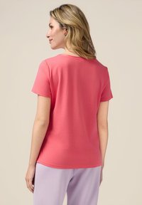Lichtroze T-shirt met korte mouwen en een ronde hals. Zachte katoenen stof, relaxte pasvorm en eenvoudige stikseldetails. Draagt bij een lavendelbroek.