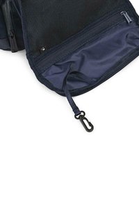 Bolsa de malla azul marino con interior de tela suave, que cuenta con un cierre de cremallera y un pequeño clip negro adjunto a un lazo de tela en el interior.