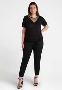 Czarny krótki top z lekko przezroczystym dekoltem w kształcie litery V, zestawiony z czarnymi dopasowanymi spodniami i sandałkami na obcasie. Gładka tekstura, minimalne akcenty.