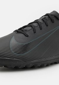 Lähedalt vaade mustale tekstureeritud Nike spordijalatsile, millel on paelad ja tume swooshi logo külgedel, loodud välistingimustes kasutamiseks.