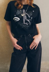 Black cotton t-shirt featuring a gray graphic of a basketball player, accented with stars and a net design. Paired with high-waisted denim jeans.