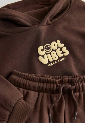 Brauner Hoodie mit einer Vorderasche, versehen mit einem cremefarbenen Schriftzug "COOL VIBES" und einem Smiley-Gesicht. Weicher, strukturierter Stoff.