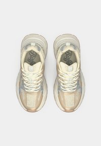 Bézs és szürke sportcipők hálós panelekből, vastag talpakkal és kontrasztos, texturált részletekkel. Fehér fűzőkkel és logó díszítésekkel.