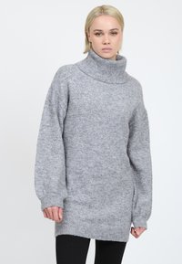 Grå strikket sweater med høj funnel neck, lange ærmer, ribbede manchetter og en let oversized pasform, der har en blød, struktureret finish.