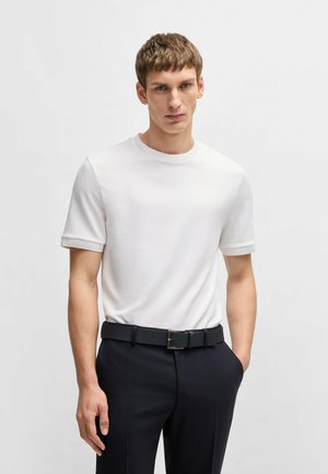 T-shirt bianco a maniche corte con collo rotondo, realizzata in tessuto testurizzato, abbinata a pantaloni scuri su misura e una cintura nera con fibbia rettangolare.