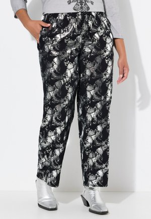 Zwarte broek met een metallic zilveren abstract patroon, elastische tailleband, zijzakken en een losse pasvorm, gecombineerd met zilveren enkellaarsjes.