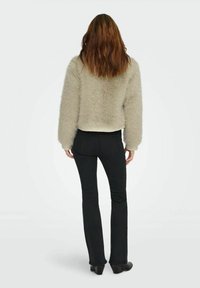 Faux fur light beige cropped jacket with long sleeves, worn over black flared jeans and heeled boots, viewed from the back.