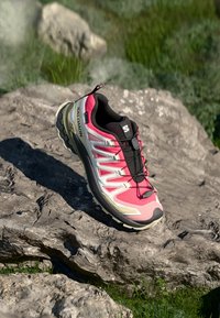 Running shoe with a pink and gray upper, black accents, and a textured sole. Features a lacing system and a cushioned collar.